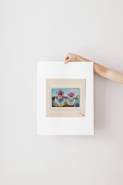 A person's hand is holding a white picture frame with a framed image of two cartoon characters inside it.