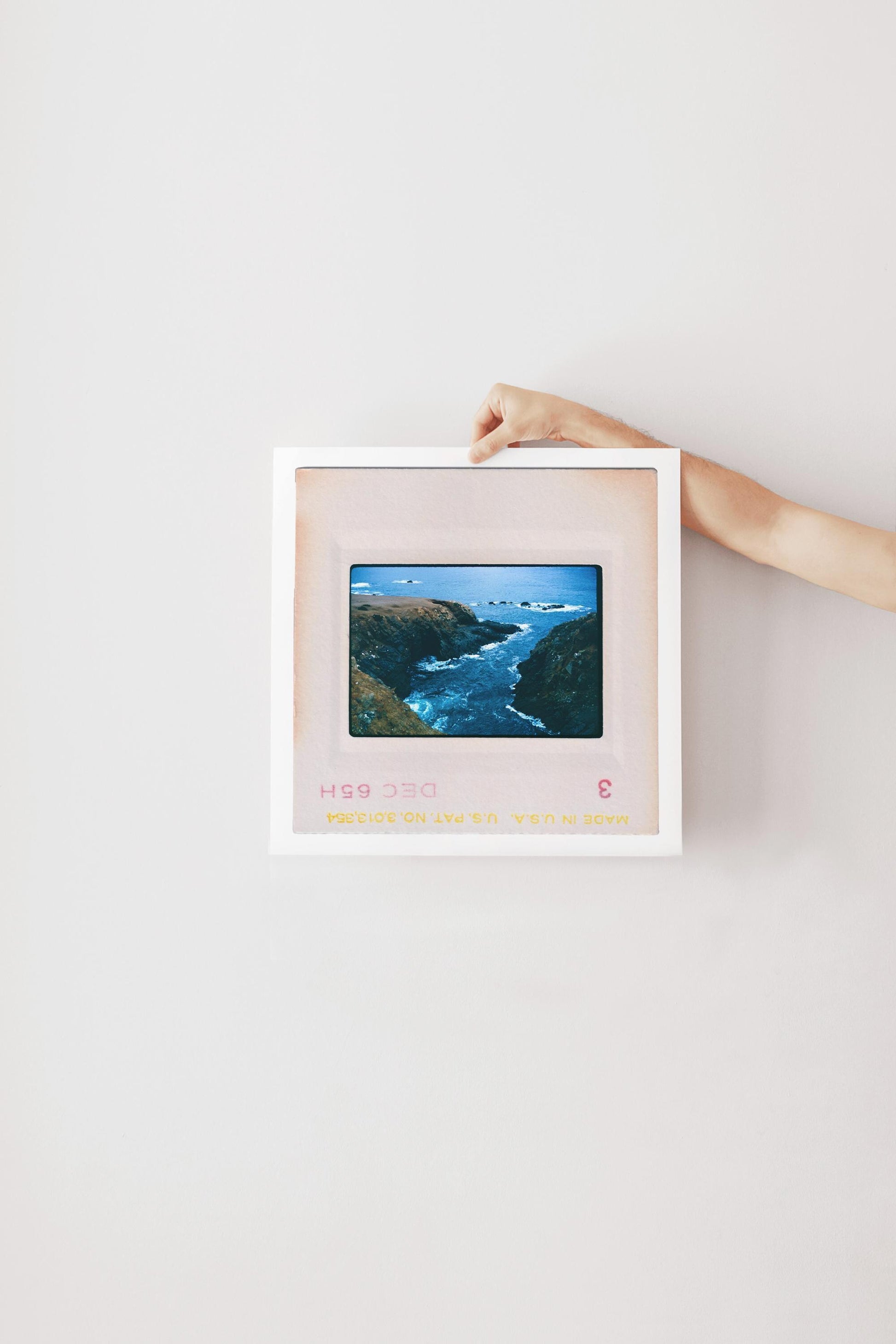Vintage 1965 Kodachrome slide photograph taken from an elevated vantage point looking down into a narrow rocky inlet along the California coast, with deep teal water churning between two rugged headlands and scattered rocks visible in the open Pacific Ocean beyond. Printed as a giclée fine art print on archival matte paper.