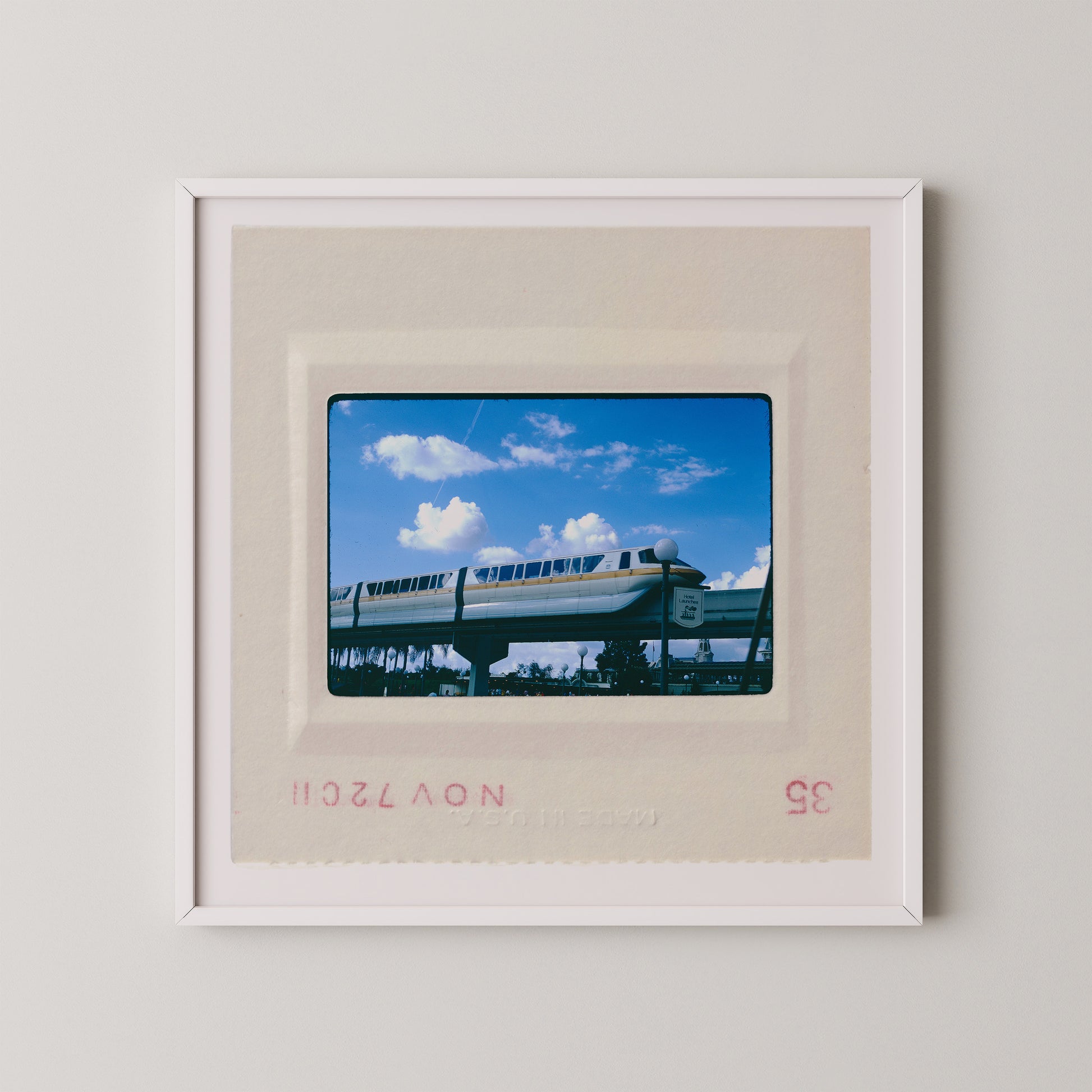 A framed photograph of a monorail train on a track against a blue sky with clouds.
