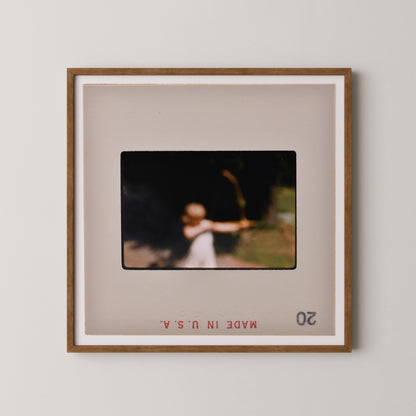 The image is a framed photograph of a person holding a bow and arrow, with the text "MAKE IT IN" visible at the bottom of the frame.