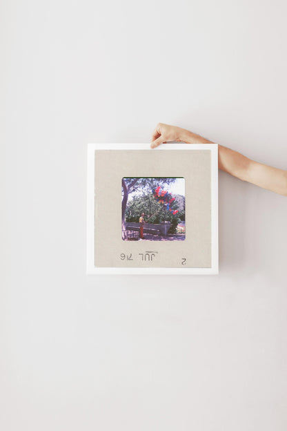 A hand is holding a framed photograph of a tree with red flowers against a white background.