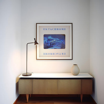 a corner of a room with a wooden cabinet, a lamp, and a framed picture hanging on the wall.