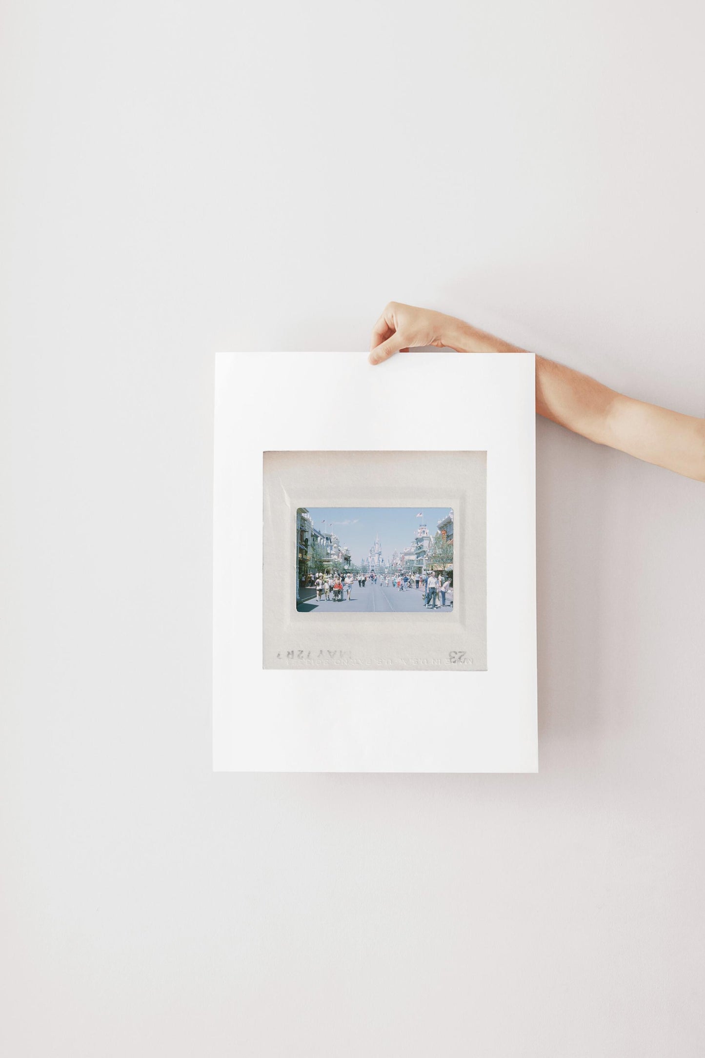 A person's hand is holding a white picture frame with a photograph of a city street visible through the frame.