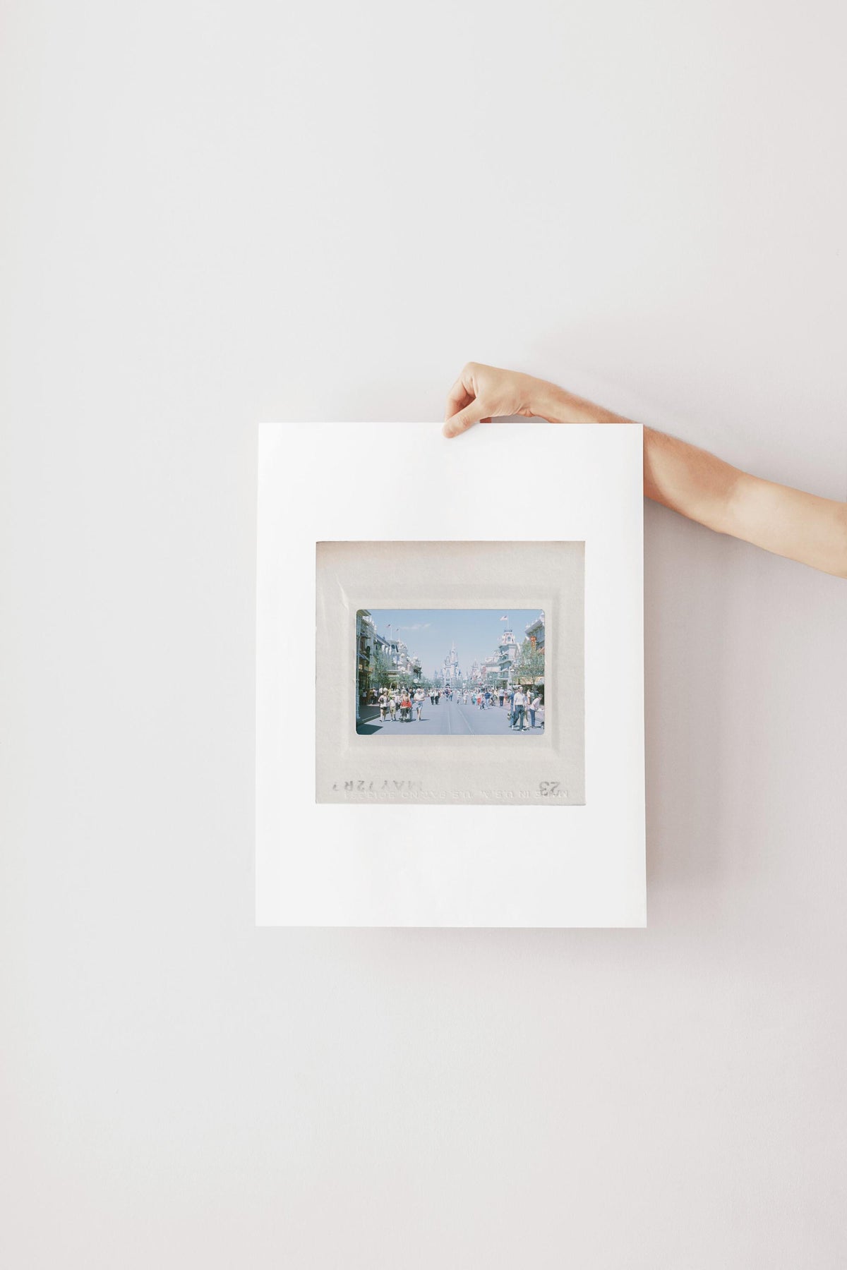 A person's hand is holding a white picture frame with a photograph of a city street visible through the frame.