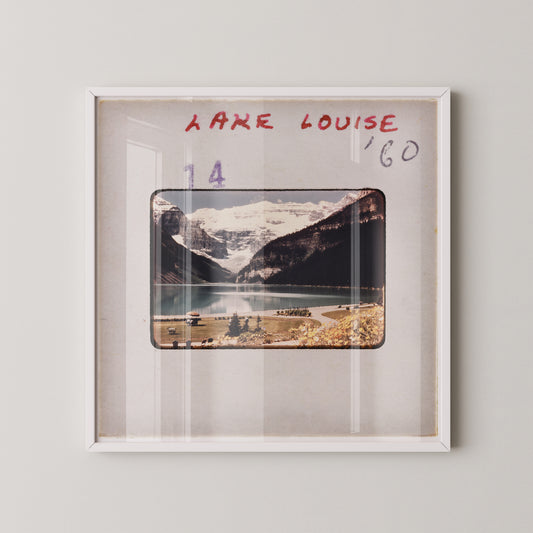 The image is a framed photograph of a scenic mountain landscape, with a lake and snow-capped peaks in the background.