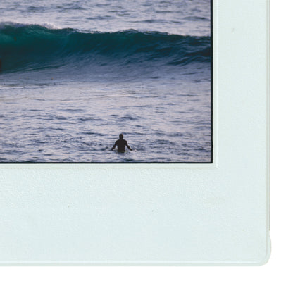 A person is seen swimming in the ocean, with a large wave crashing behind them.