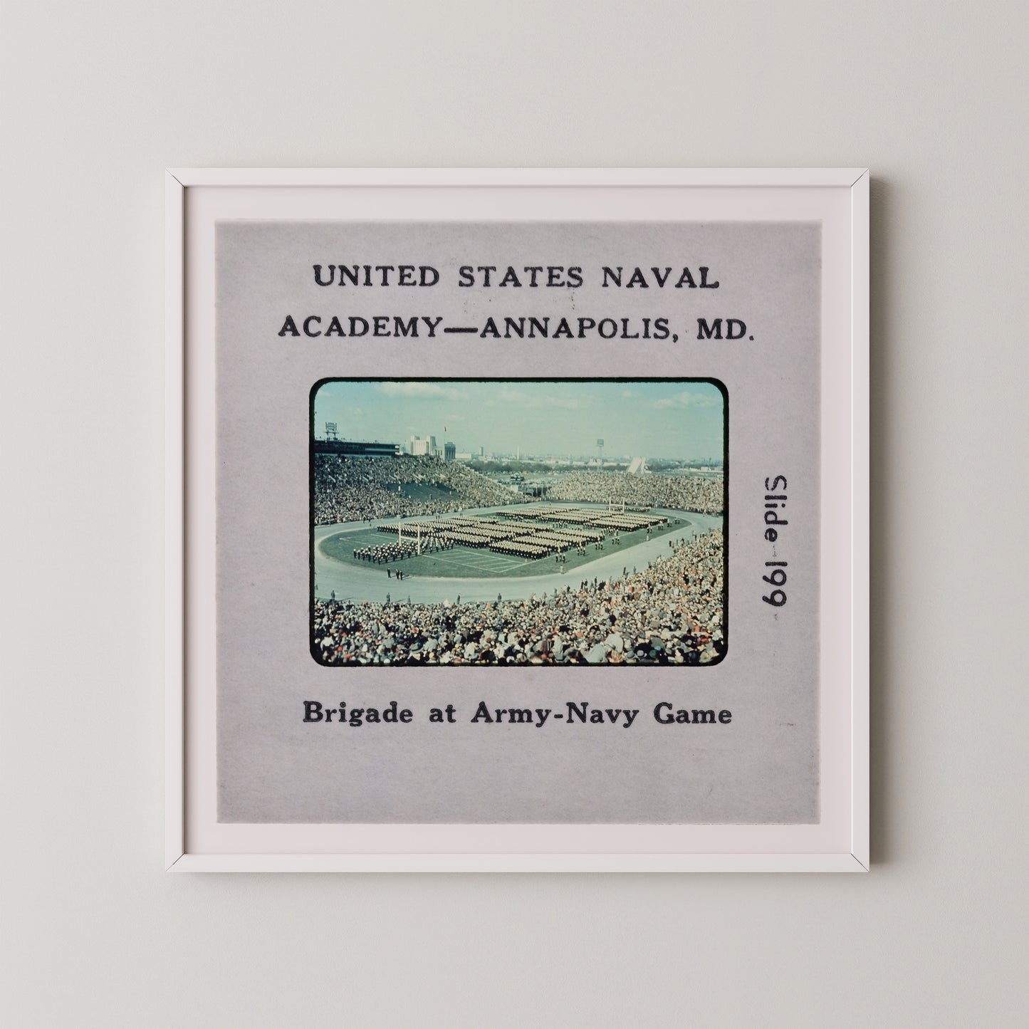 The image is a framed photograph of a large crowd at an Army-Navy game, with a military parade taking place in the background.