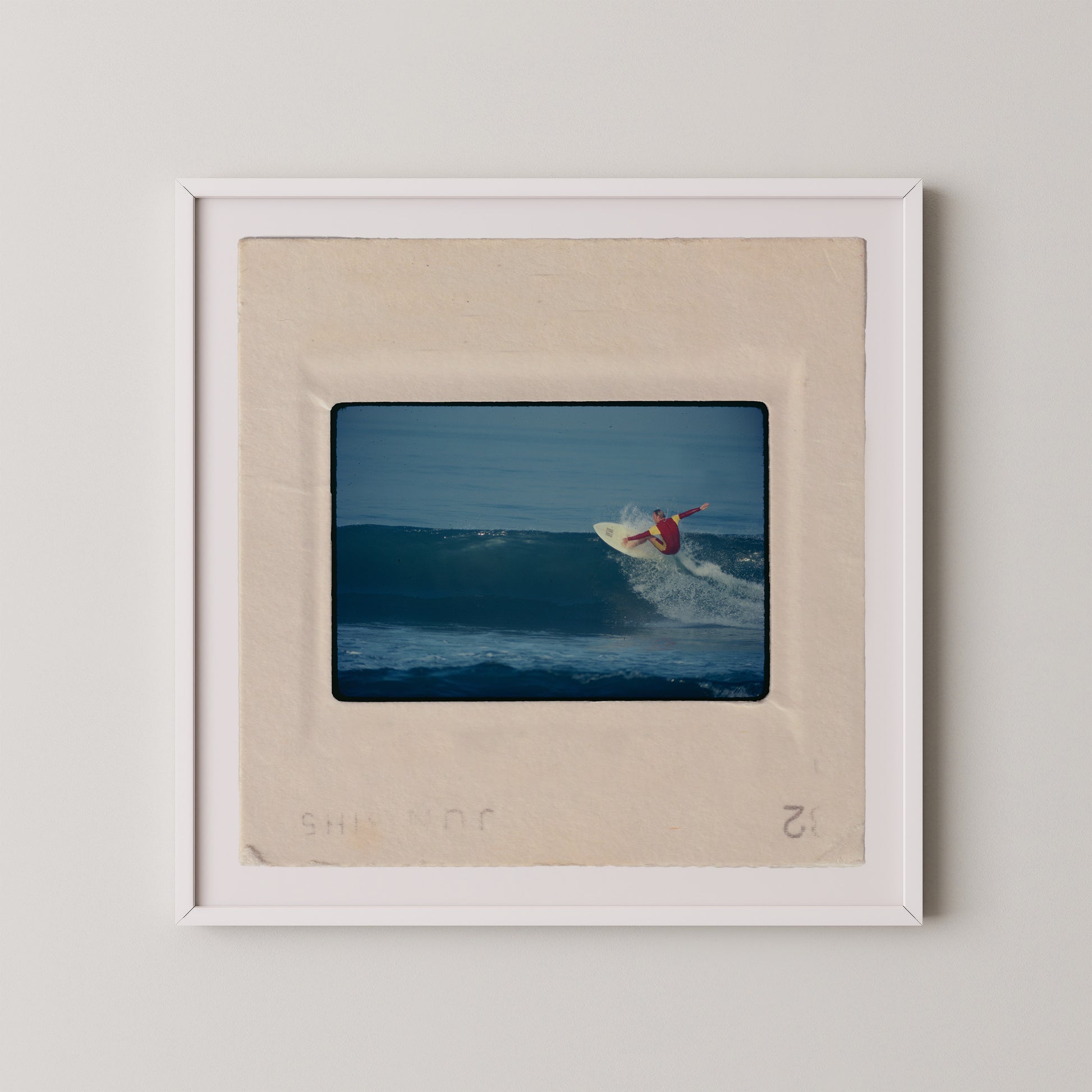 A framed photograph of a surfer riding a wave, with the surfer wearing a red shirt and the wave appearing to be a deep blue color.