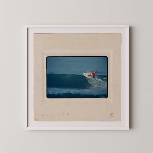 A framed photograph of a surfer riding a wave, with the surfer wearing a red shirt and the wave appearing to be a deep blue color.