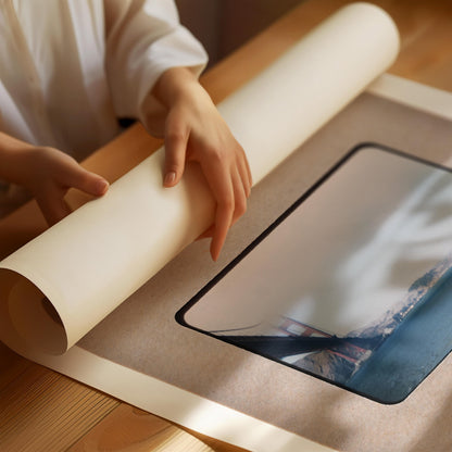 A person's hands are holding a roll of paper over a printed image on a wooden surface.