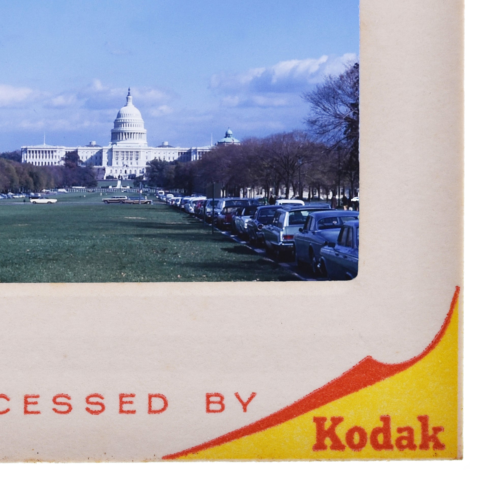 a large white building with a dome, likely the United States Capitol building, with a row of parked cars in the foreground.