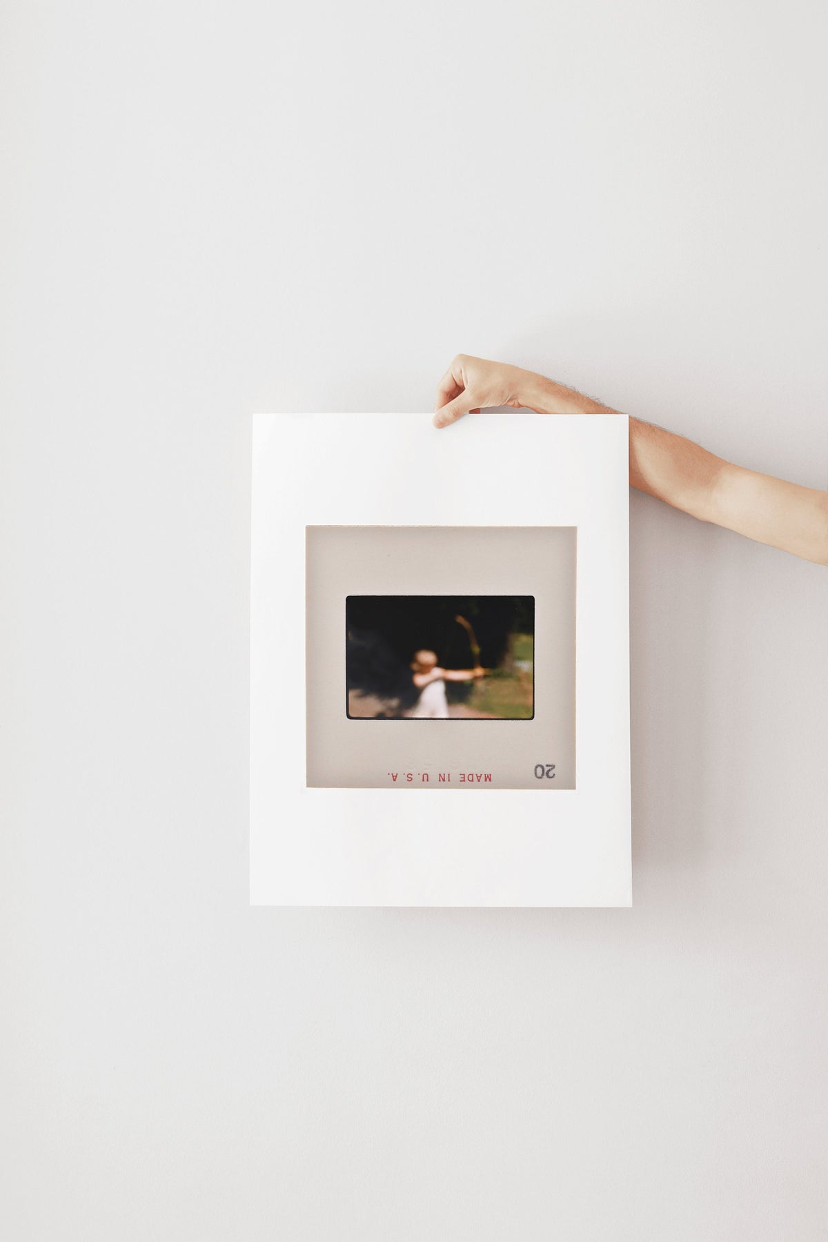 A person's hand is holding a white picture frame with a photograph inside it, against a plain white wall.