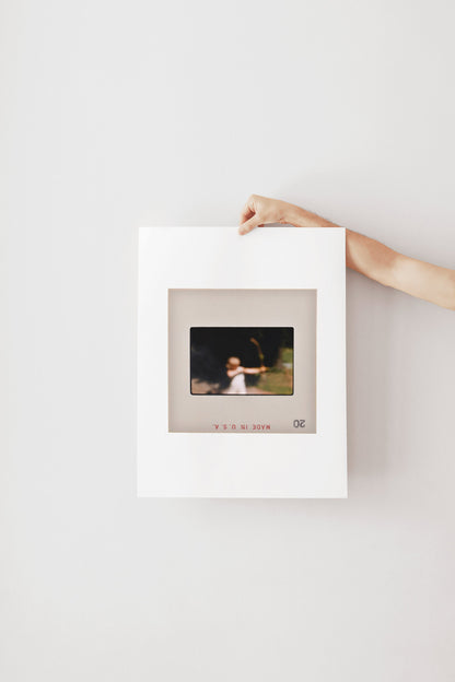 A person's hand is holding a white picture frame with a photograph inside it, against a plain white wall.