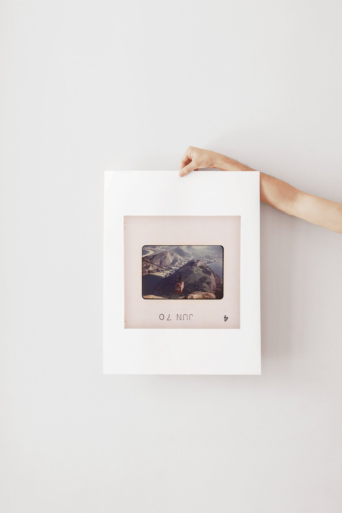 A person's hand is holding a white picture frame with a photograph of a mountain landscape inside it.