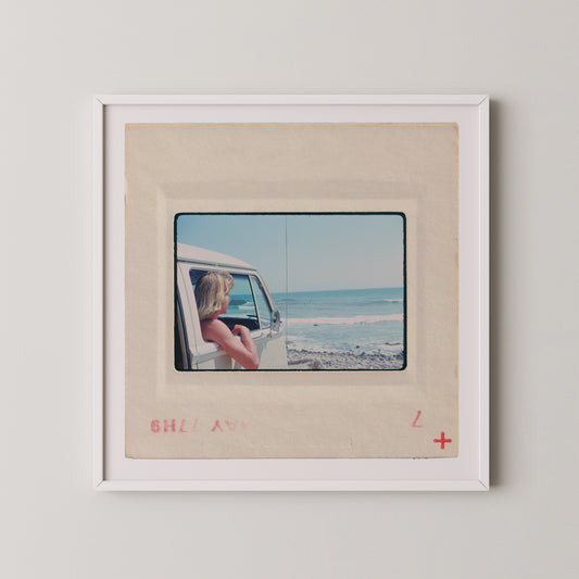 A framed photograph of a person looking out of a vehicle window at the ocean.