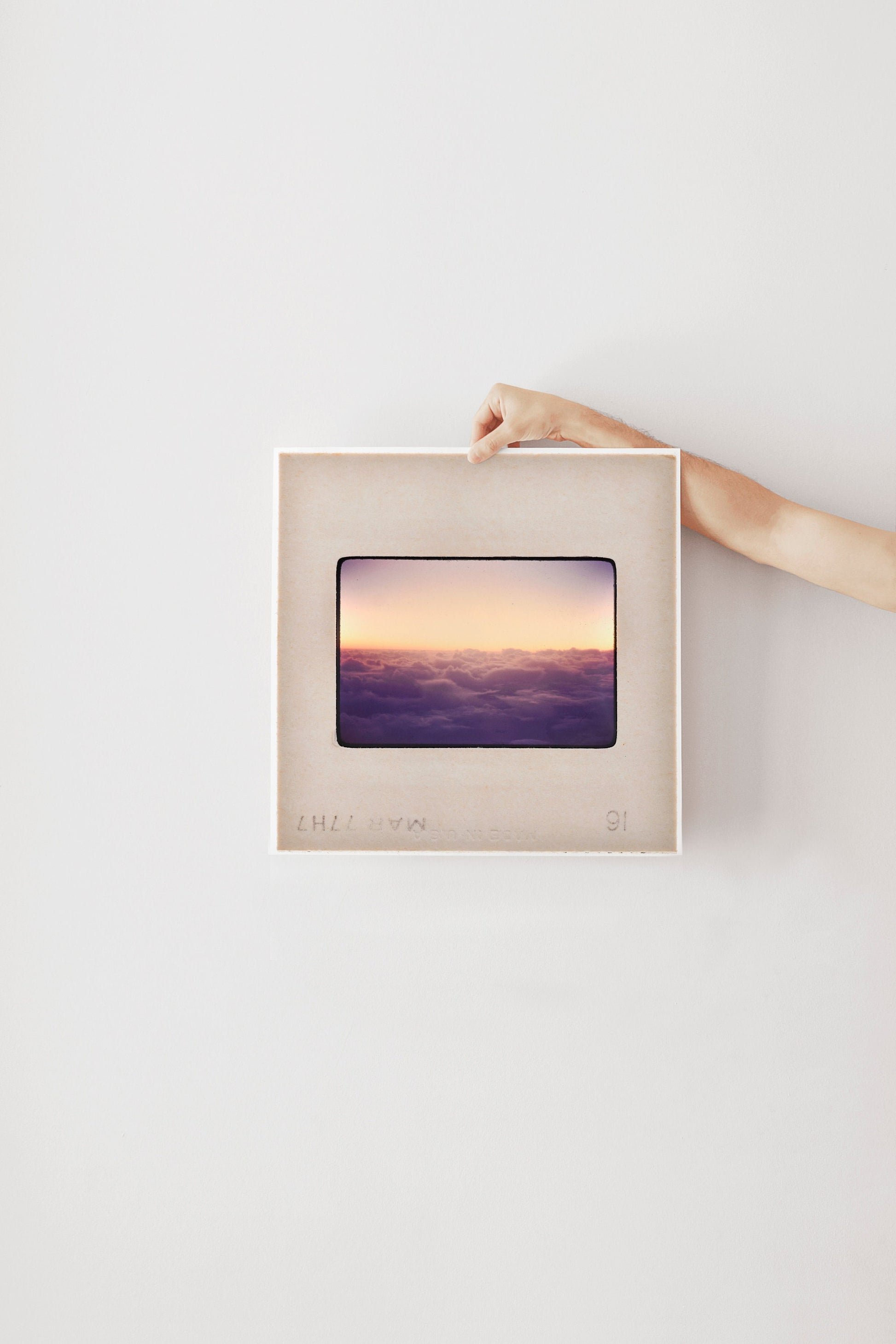 A person's hand is holding a framed picture of a sunset over a body of water.