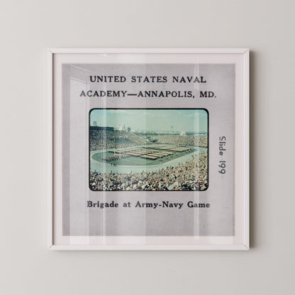 The image is a framed photograph of a crowded stadium, likely from the United States Naval Academy in Annapolis, MD, during a military parade.