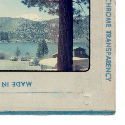 The image is a framed photograph of a snowy mountain landscape with a lake and a small building in the background.