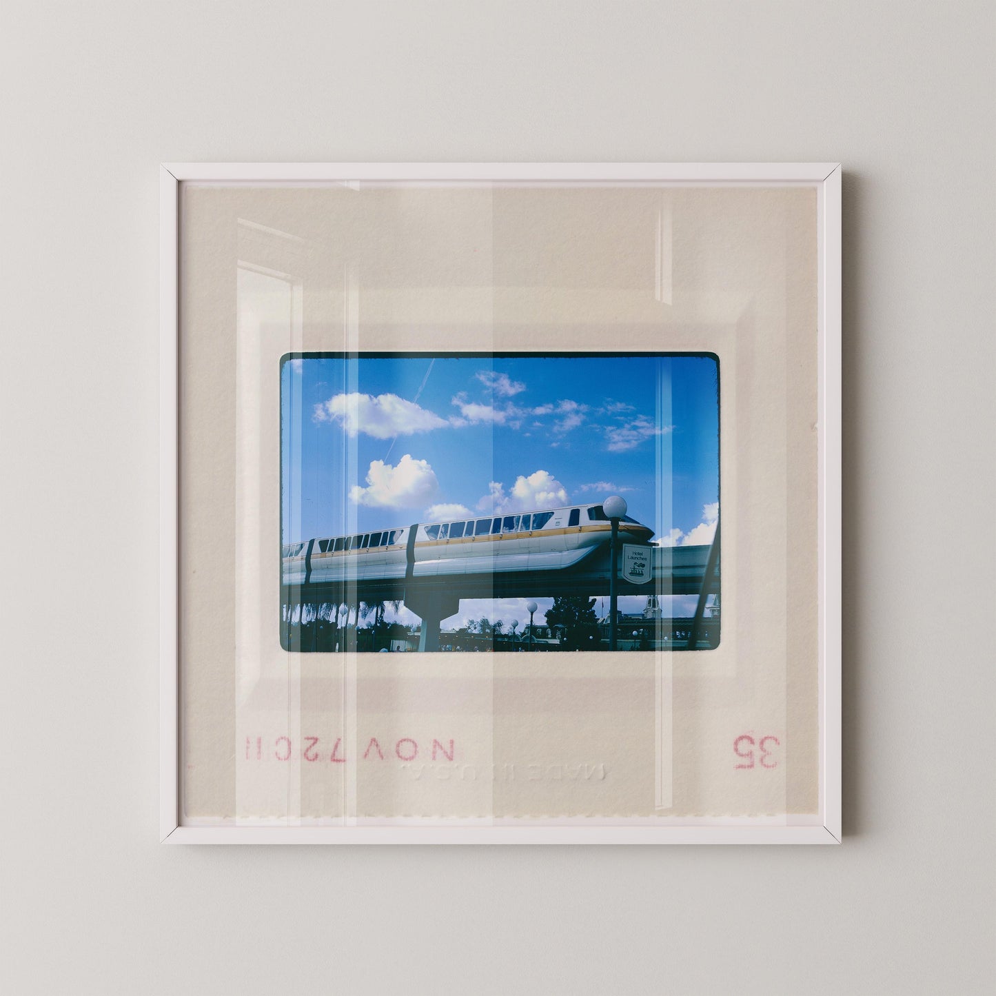 A framed photograph of a monorail train on a clear day, with a blue sky and fluffy white clouds in the background.