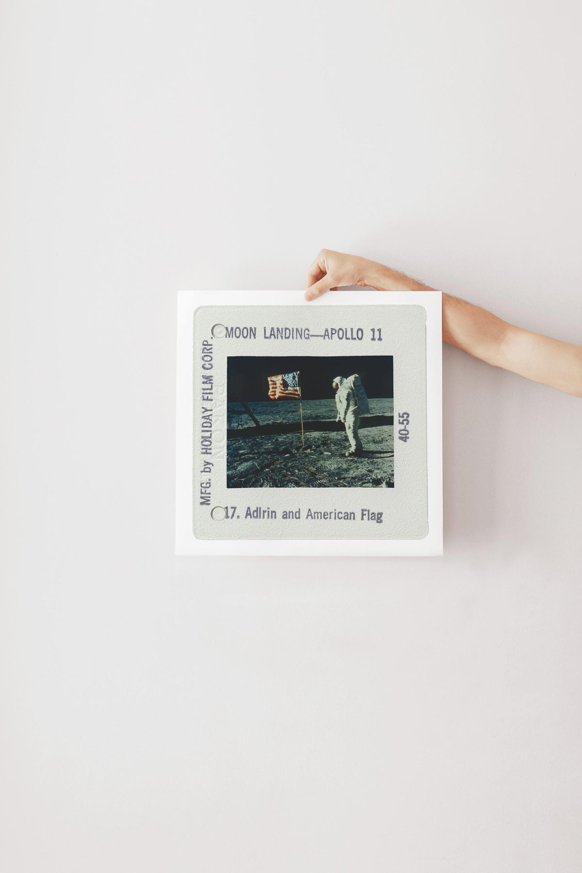 A person's hand is holding a framed photograph of the Apollo 11 moon landing, with the caption "Moon Landing - Apollo 11" and the date "C.17. Adrin and American Flag".