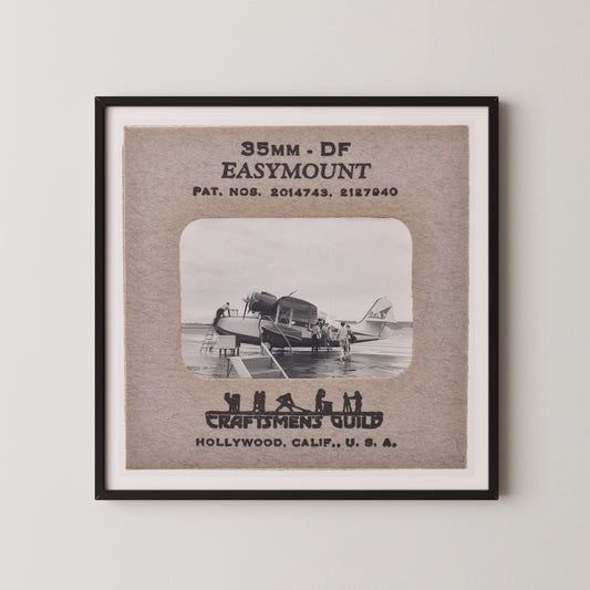 The image is a framed photograph of a vintage airplane, with text and a black and white illustration of people on the airplane.