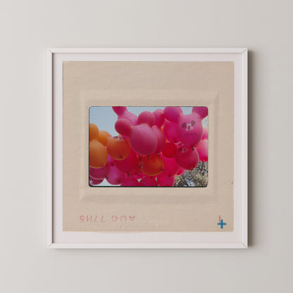 A framed photograph of a bunch of colorful balloons, including pink and orange balloons, floating in the sky.