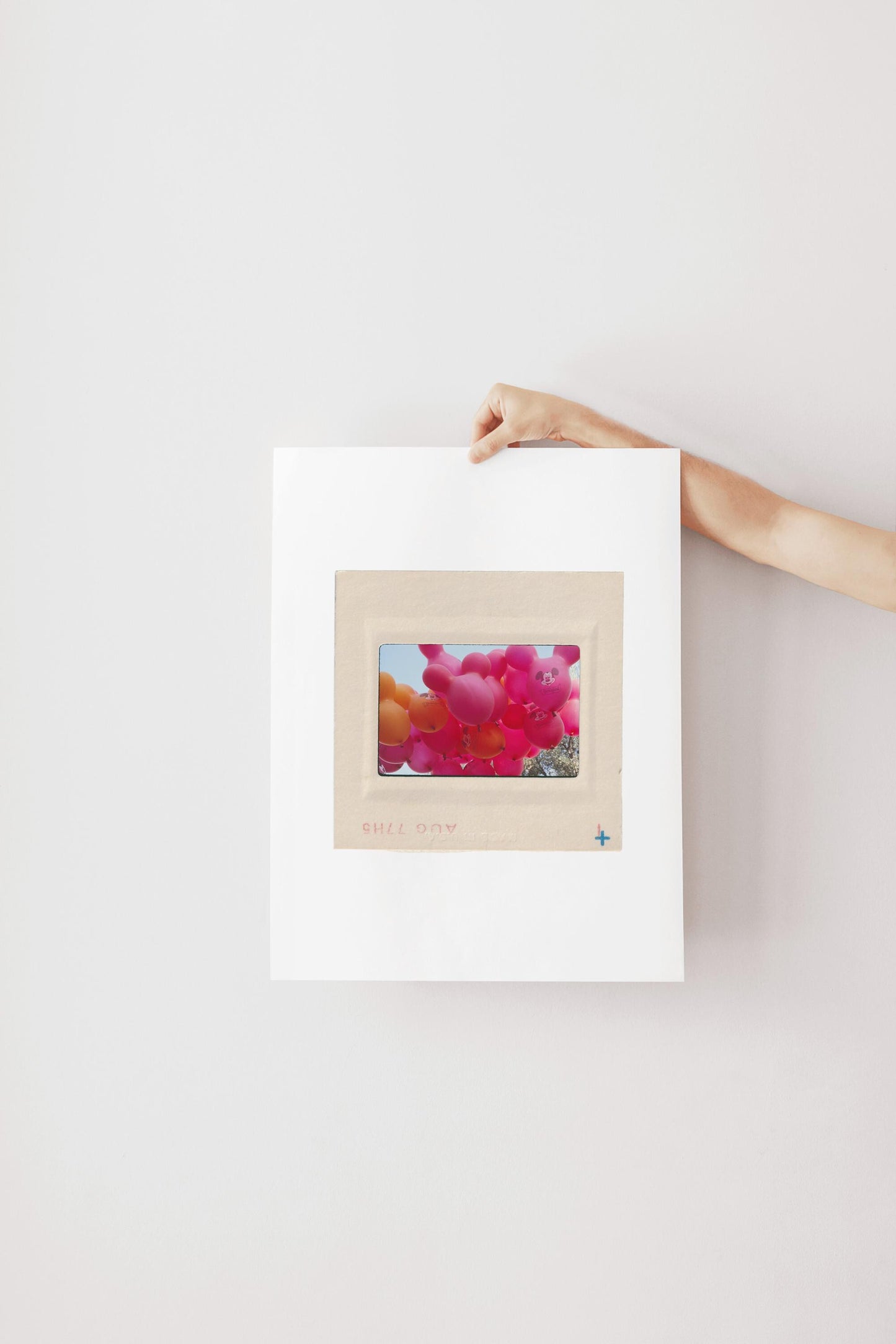 A person's hand is holding a white piece of paper with a framed image of colorful balloons on it.