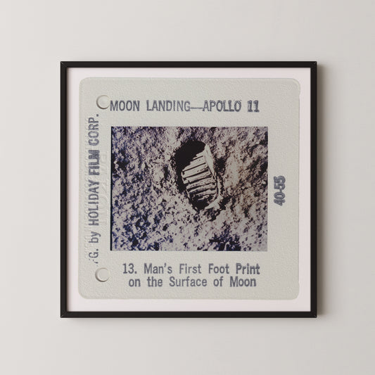The image is a framed photograph of a man's first footprint on the surface of the Moon, taken during the Apollo 11 mission.
