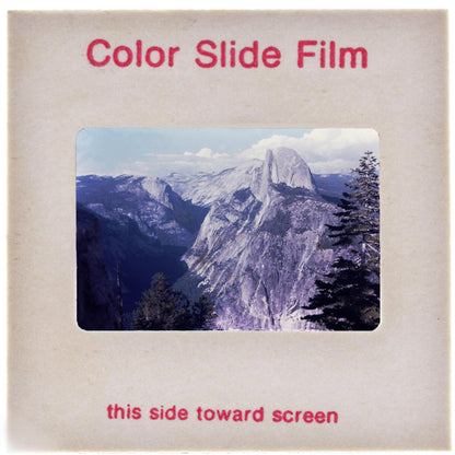 The image is a color slide film depicting a mountainous landscape with a clear blue sky and clouds.