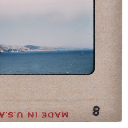 The image is a framed photograph of a scenic view of a body of water, likely the ocean, with mountains in the background.