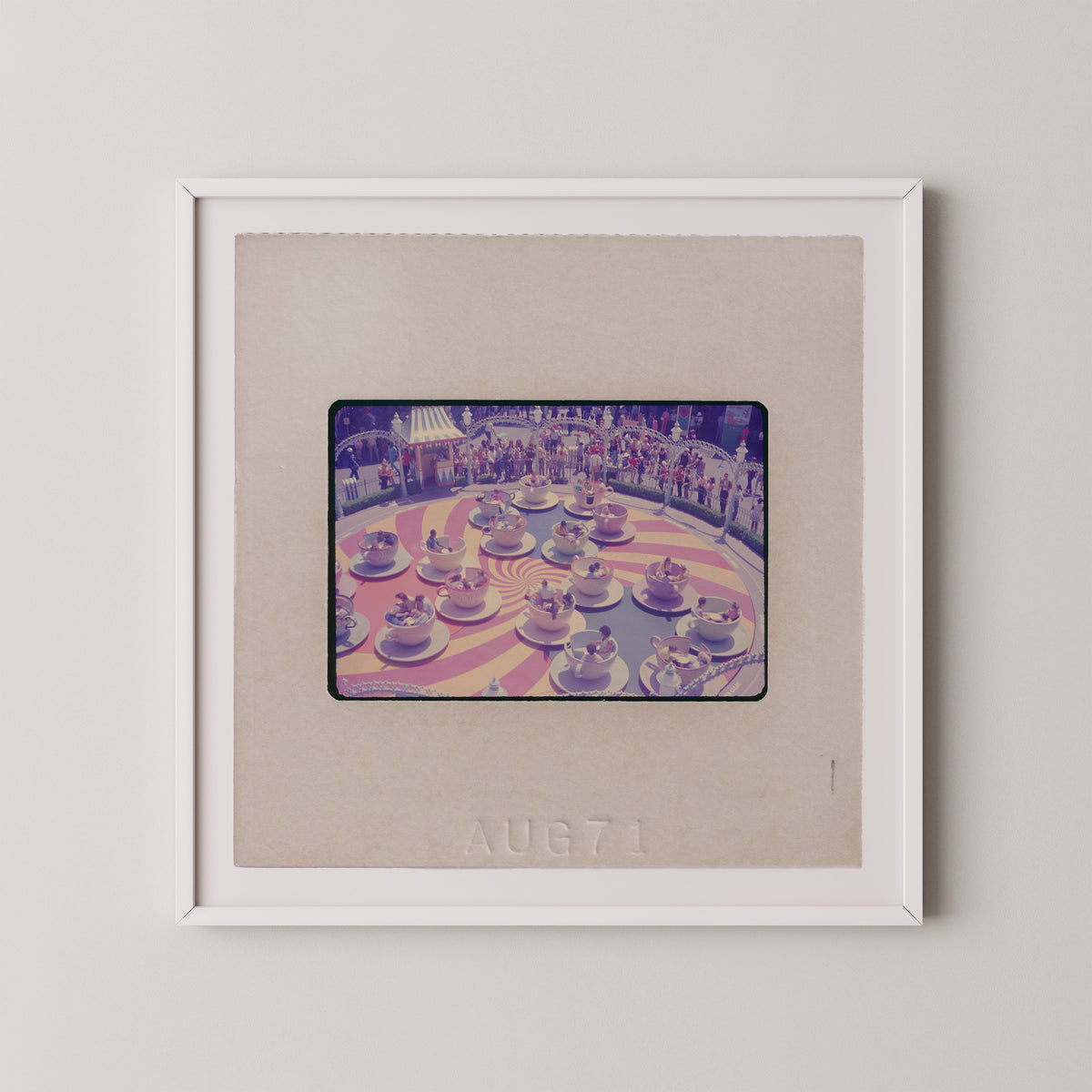 The image is a framed photograph of a carousel with multiple cars and people on it.