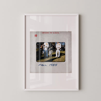The image is a framed photograph of two people standing on a grassy field, with a text overlay that reads "FALL 1955".