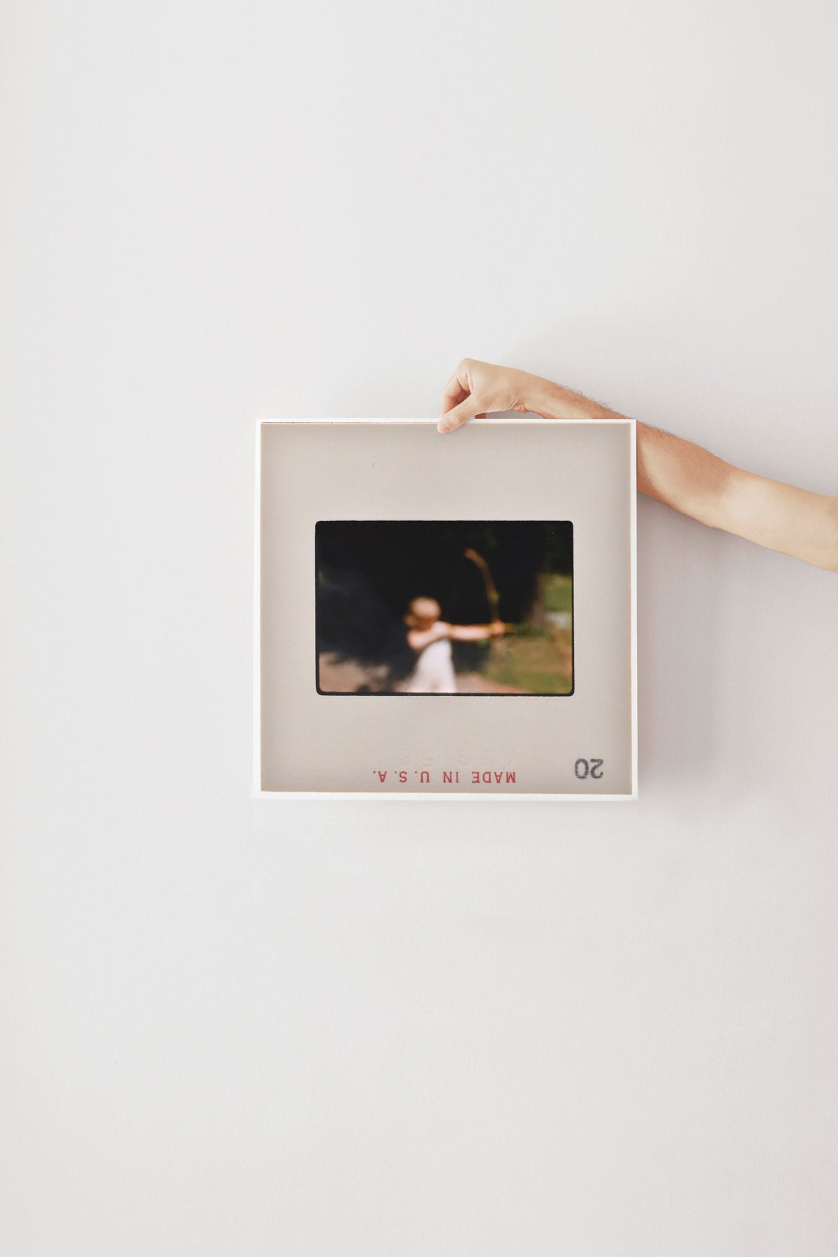 A person's hand is holding a framed photograph of a person in a field, with the text "20" visible in the bottom right corner of the frame.