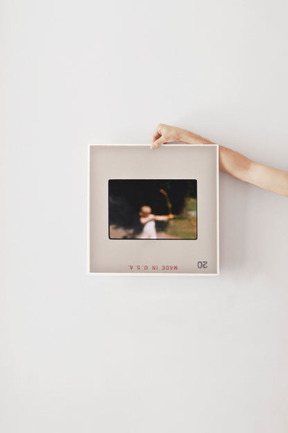 A person's hand is holding a framed photograph of a person in a field, with the text "20" visible in the bottom right corner of the frame.