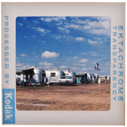 A group of camper trailers parked in a field under a blue sky with clouds.