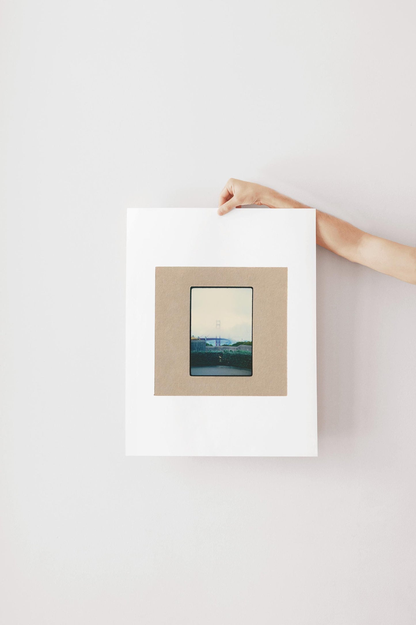 Vintage 35mm slide photograph of the Golden Gate Bridge partially obscured by dense fog, with only the tower visible above the cloud layer, viewed from a concrete overlook with green hedges in the foreground. Printed as a giclée fine art print on archival matte paper.