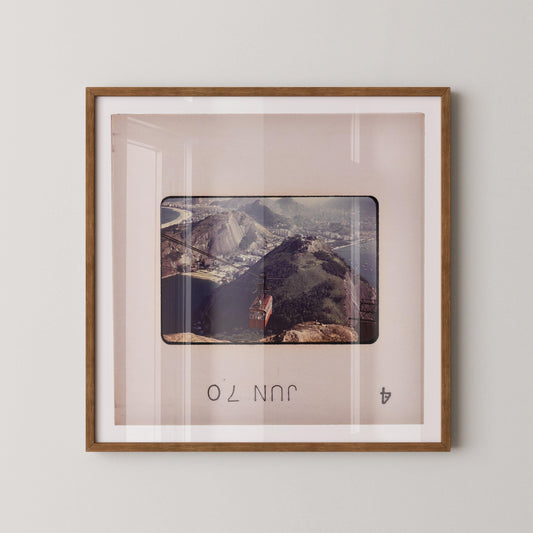 The image is a framed photograph of a mountainous landscape, with a small building visible in the distance.