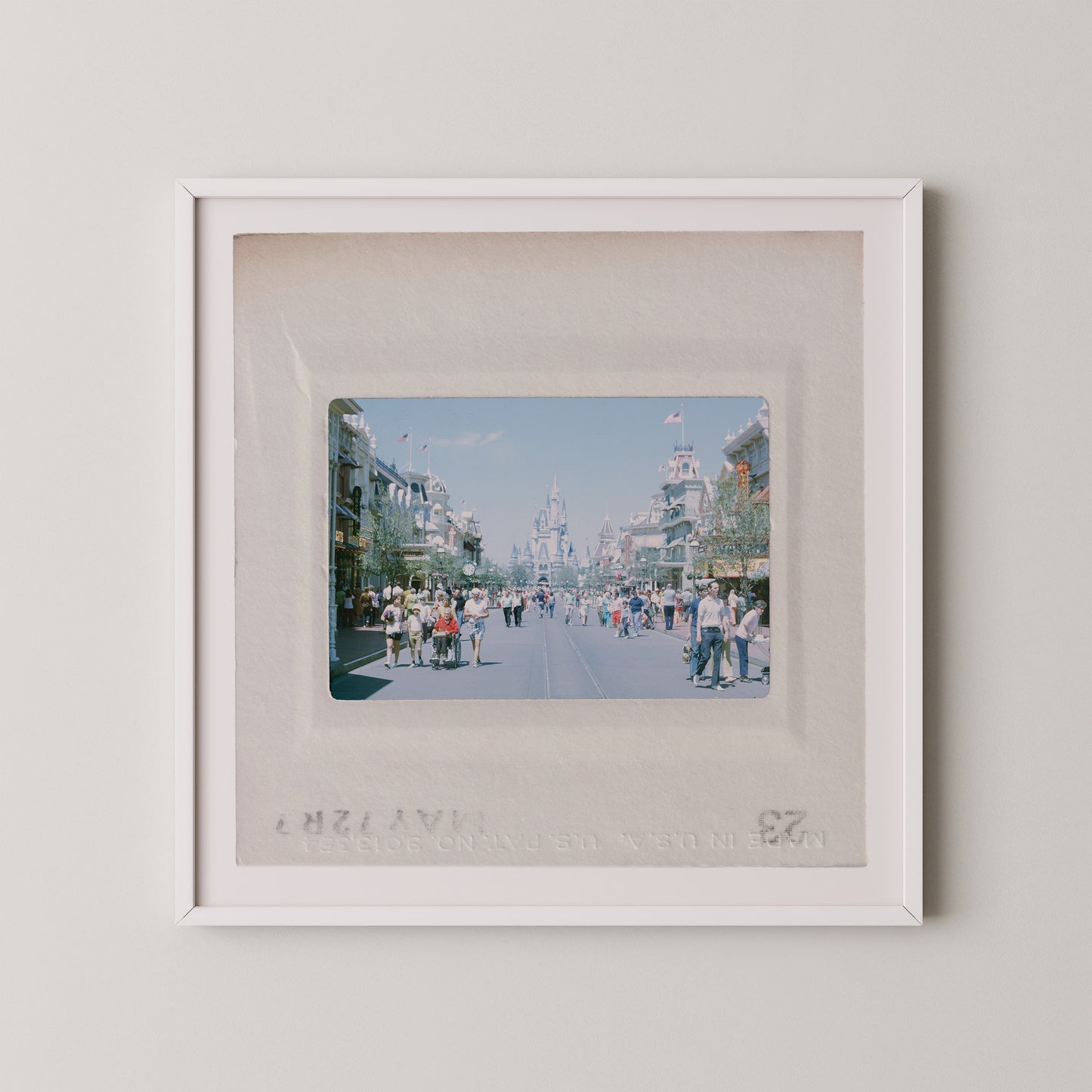 The image is a framed photograph of a busy street scene with people walking and standing on the sidewalk.
