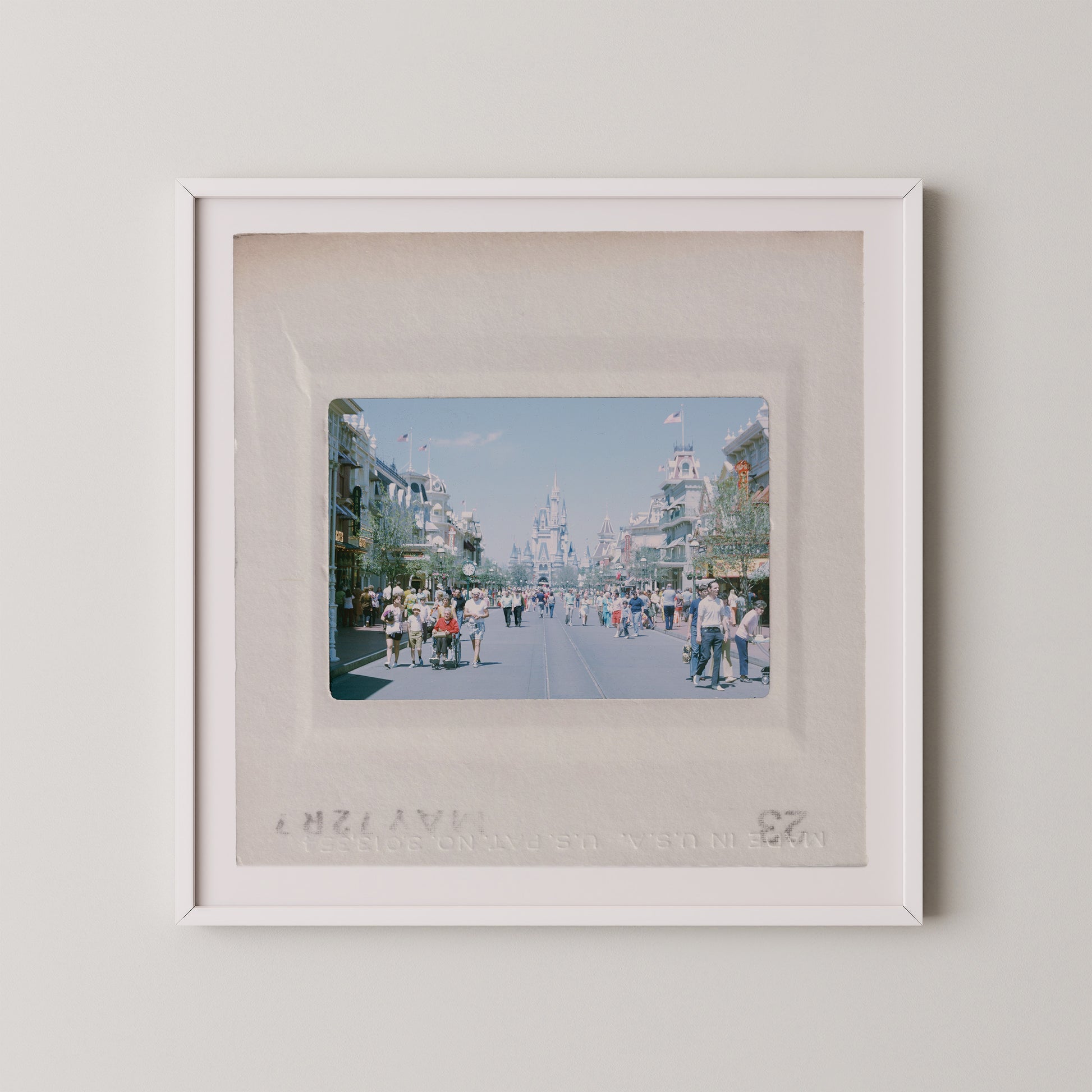 The image is a framed photograph of a busy street scene with people walking and standing on the sidewalk.