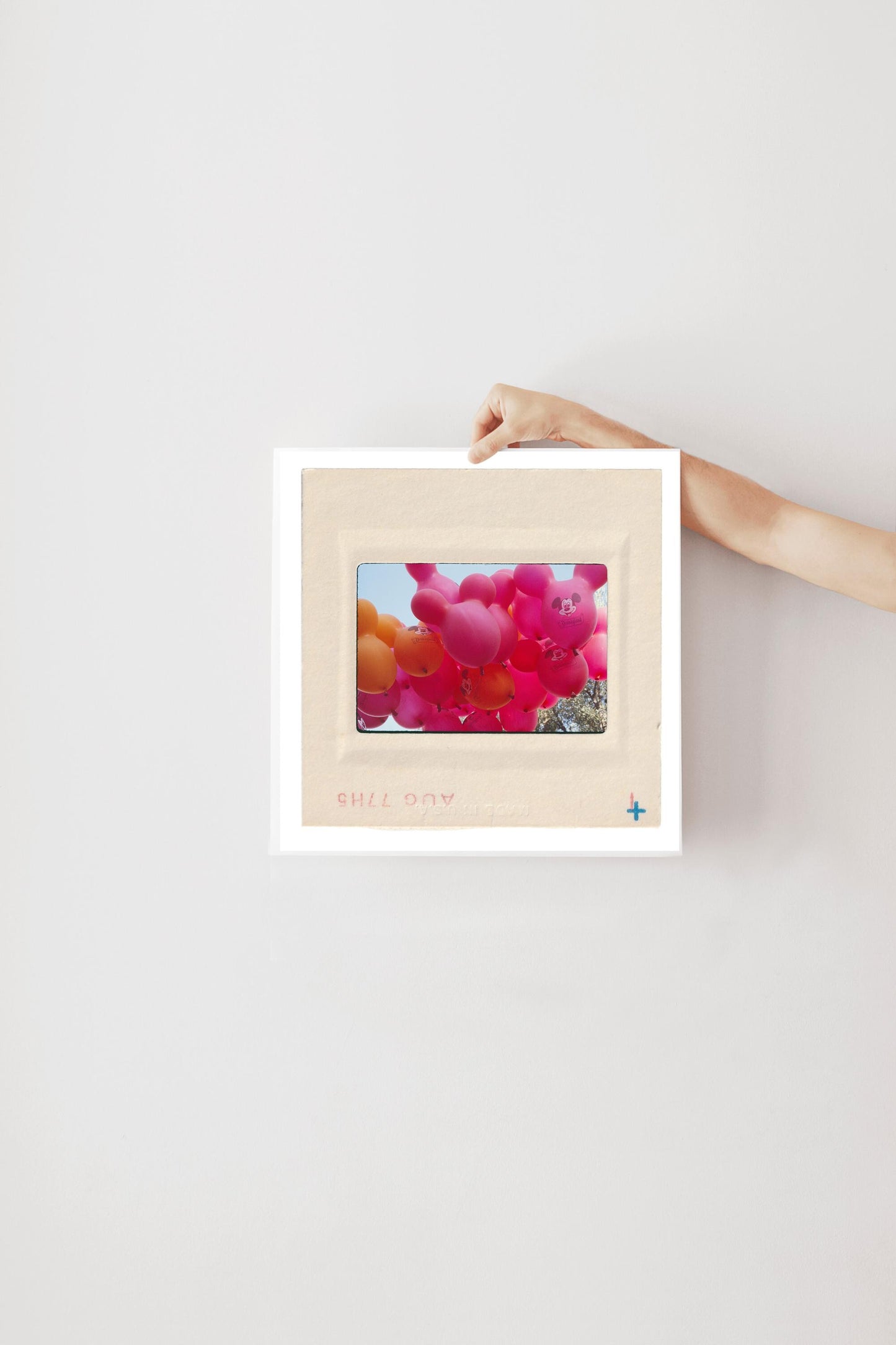 A person's hand is holding a white picture frame with a photograph of colorful balloons inside it.