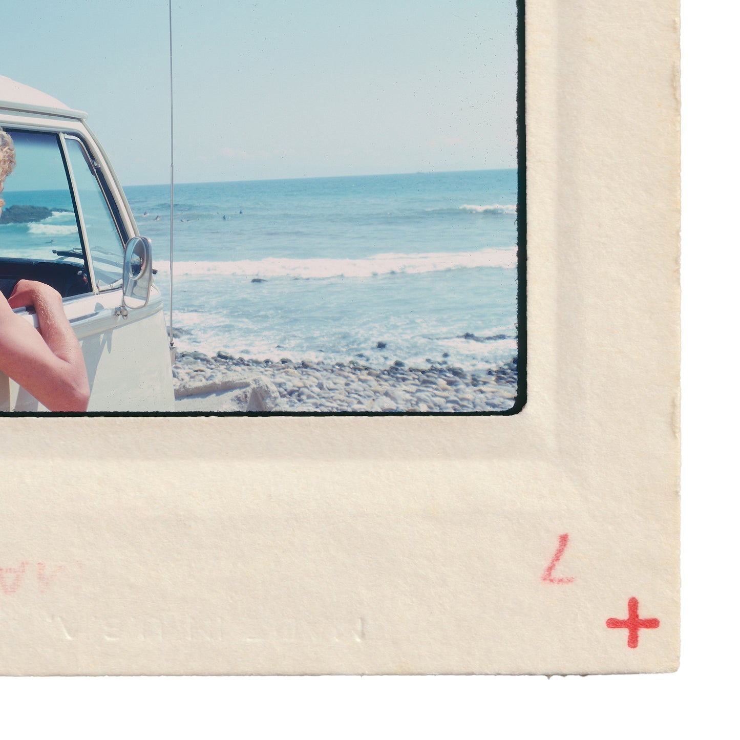 A person is sitting in a car, looking out at the ocean, with a beach and waves visible in the background.