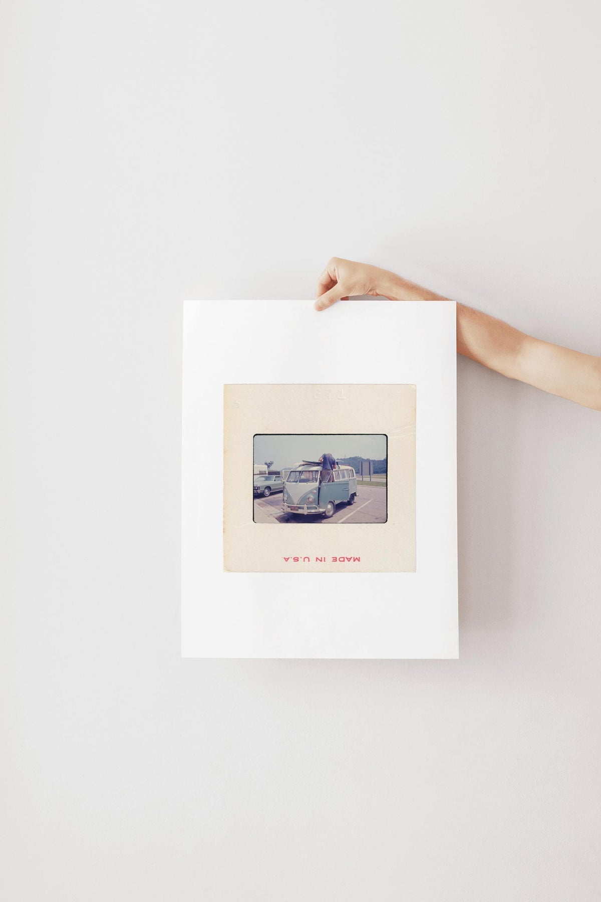 Vintage 1971 35mm slide photograph of a man loading two surfboards onto the roof rack of a pale blue Volkswagen Bus in a parking lot, with a "Welcome to Tennessee" highway sign and a vintage sedan visible in the background. Printed as a giclée fine art print on archival matte paper.