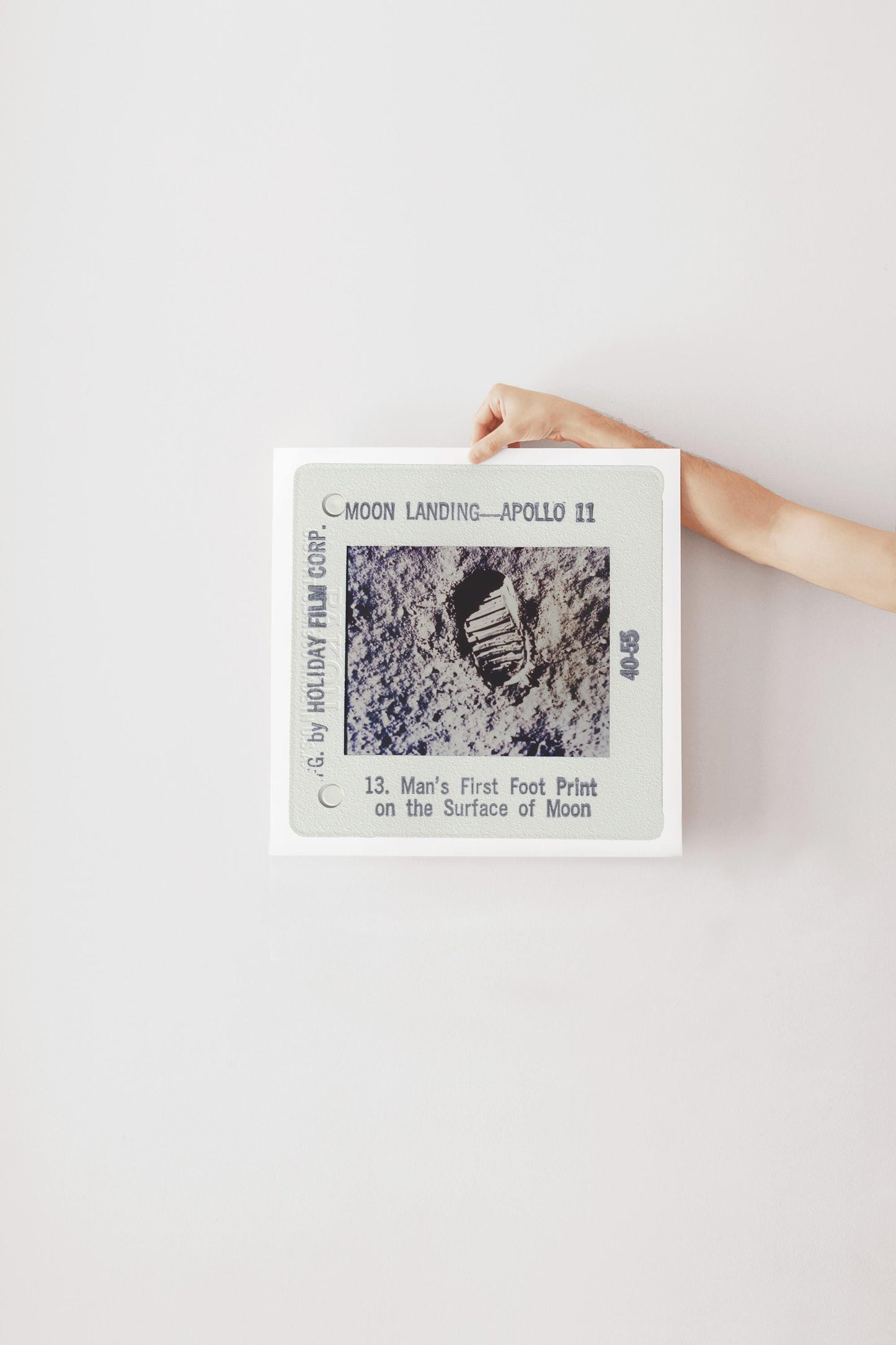 A person's hand is holding a framed photograph of a footprint on the surface of the Moon, which is labeled as "Man's First Foot Print on the Surface of Moon" and is part of the "Moon Landing - Apollo 11" series.