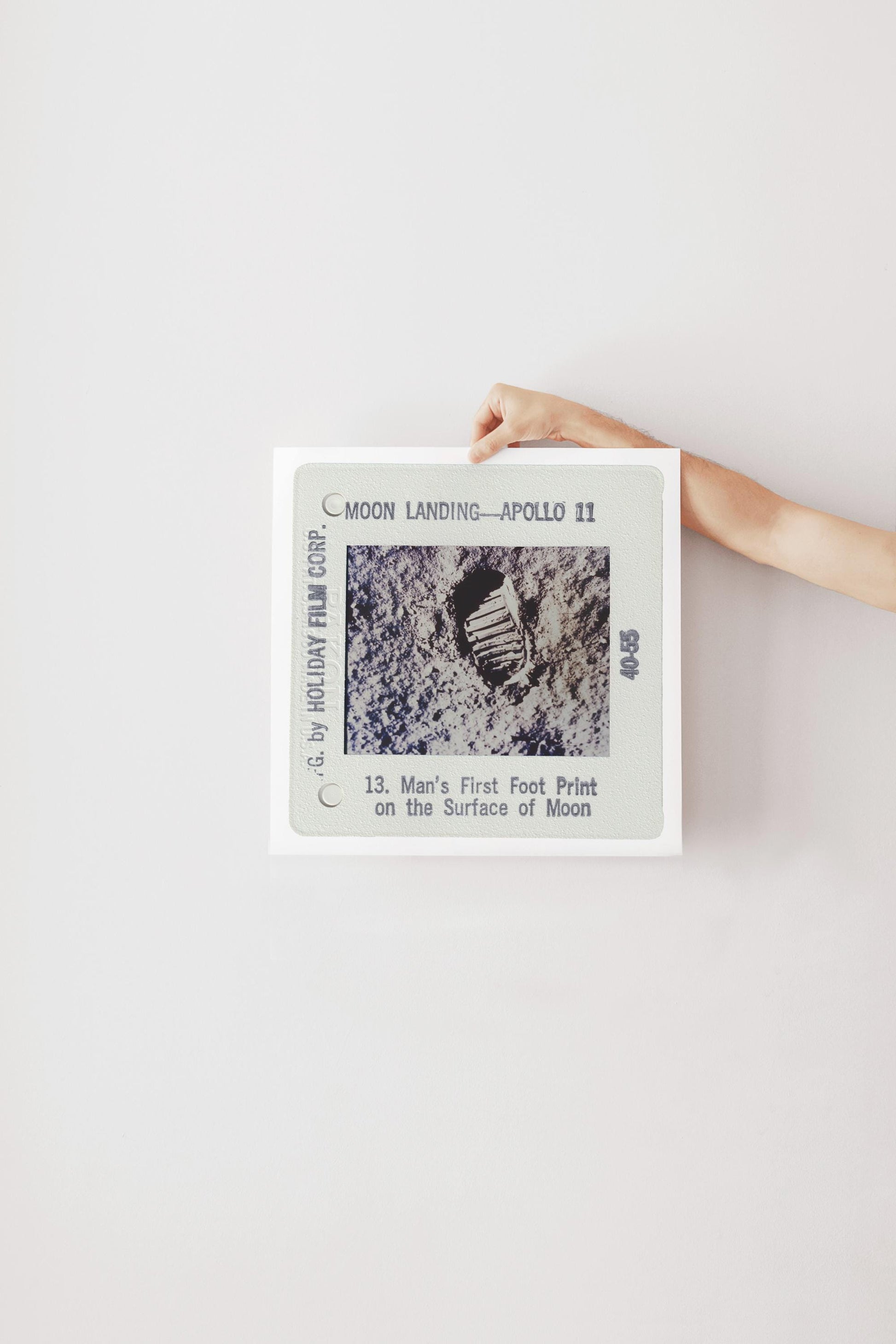 A person's hand is holding a framed photograph of a footprint on the surface of the Moon, which is labeled as "Man's First Foot Print on the Surface of Moon" and is part of the "Moon Landing - Apollo 11" series.