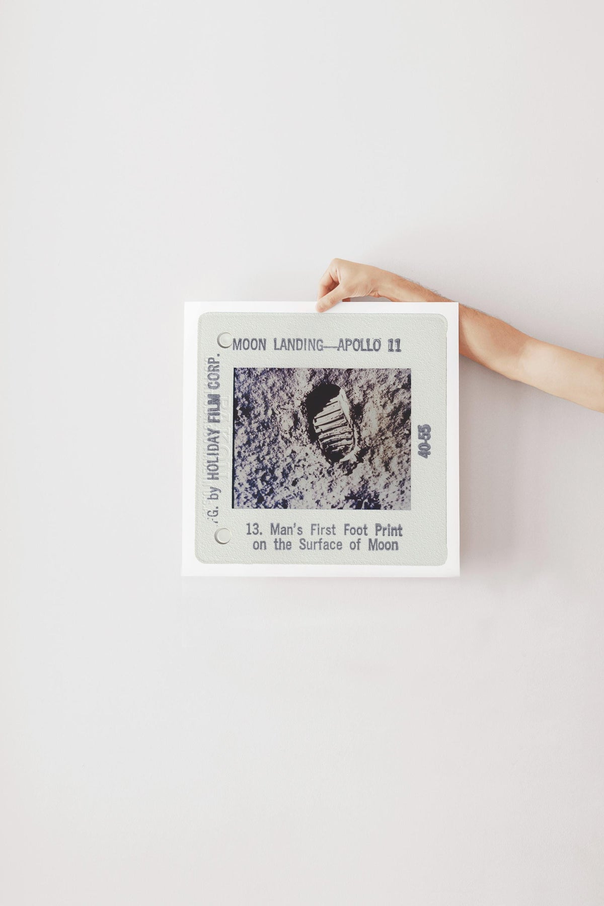 A person's hand is holding a framed photograph of a footprint on the surface of the Moon, which is labeled as "Man's First Foot Print on the Surface of Moon" and is part of the "Moon Landing - Apollo 11" series.