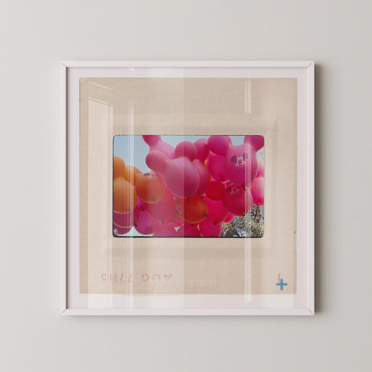 A framed photograph of a bunch of colorful balloons, including pink and orange balloons, floating in the air.