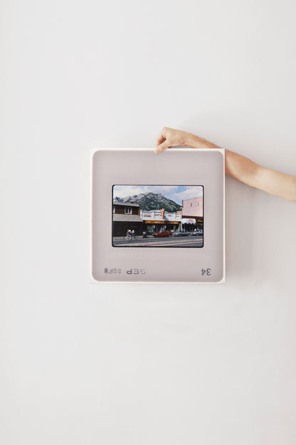 A person's hand is holding a framed photograph of a building with a mountain in the background.