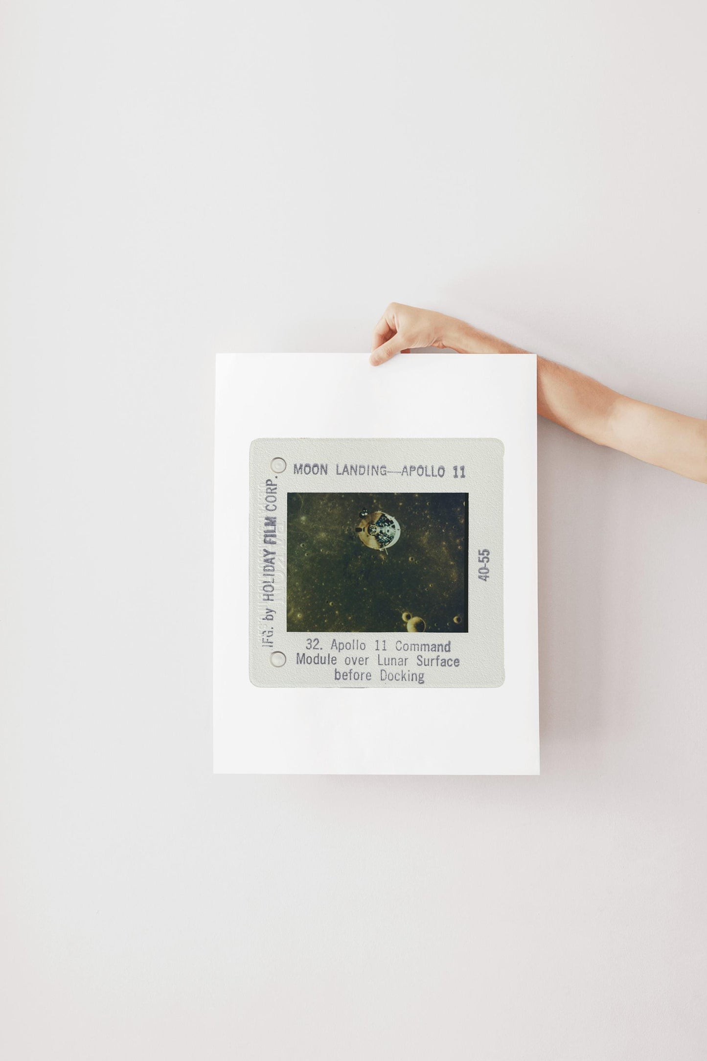 A person's hand is holding a framed photograph of the Apollo 11 moon landing, with the text "Moon Landing - Apollo 11" visible.