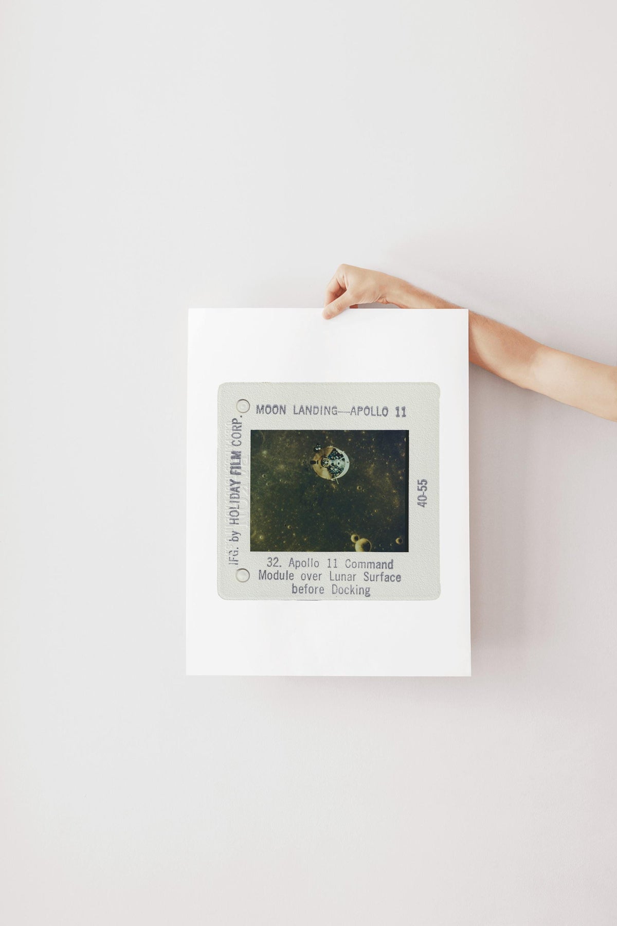 A person's hand is holding a framed photograph of the Apollo 11 moon landing, with the text "Moon Landing - Apollo 11" visible.