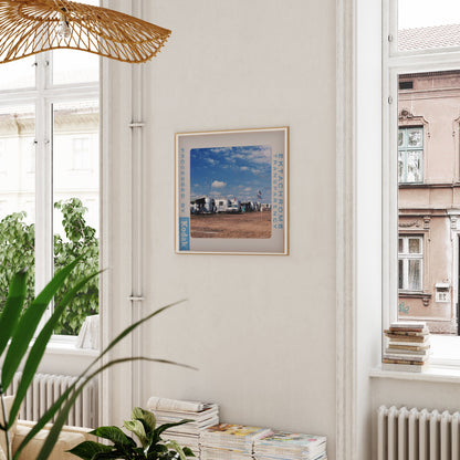a framed photograph of a beach scene hanging on a wall, with a window and a plant visible in the foreground.